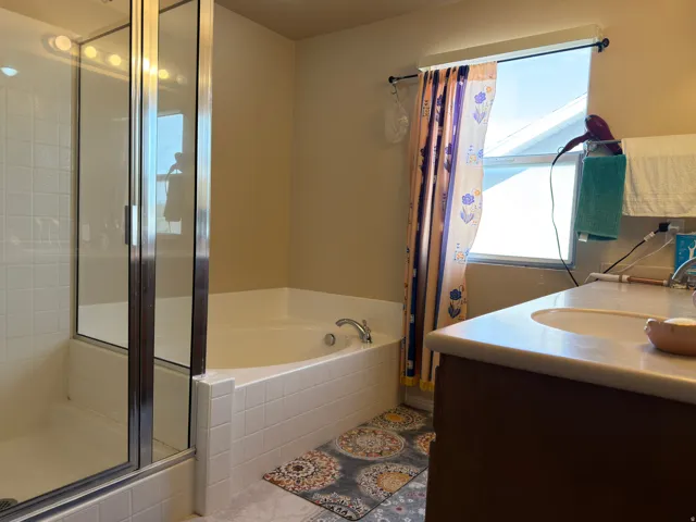 Glass-enclosed shower, jetted soaking tub, single vanity with integrated sink, window with natural light, and tile flooring