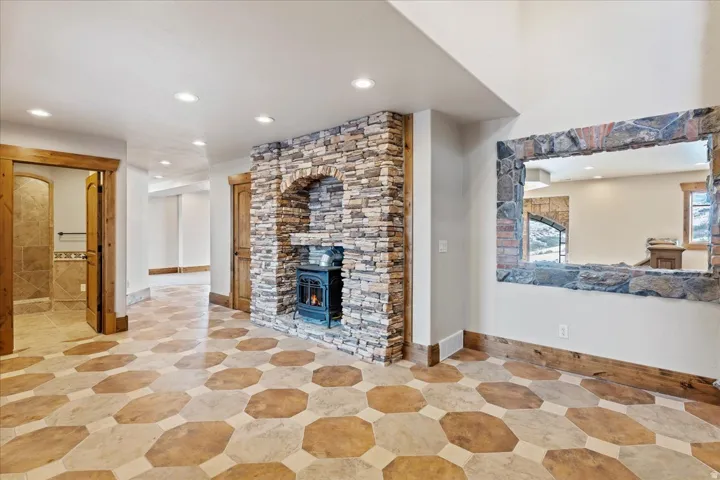 Stone-clad fireplace with hearth, recessed lighting, wood-finish trim, and unique hexagonal tile flooring