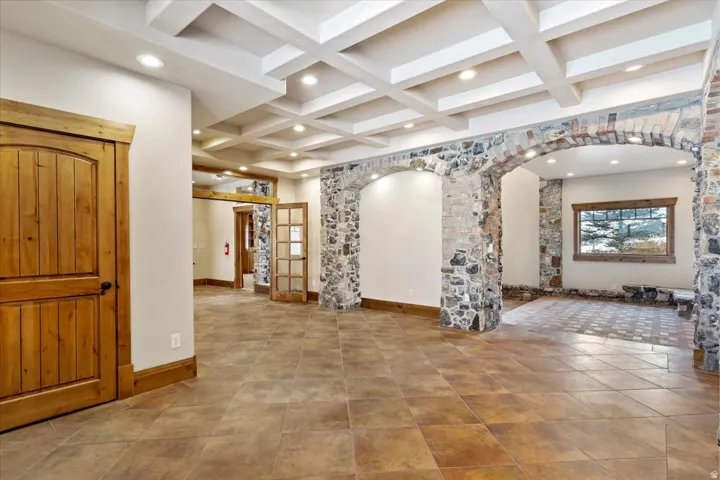 Coffered ceiling with recessed lighting, stone archways, wood-finish flooring, solid wood doors, and a built-in window bench