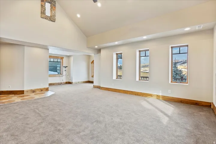 Spacious carpeted room featuring a vaulted ceiling with recessed lighting, wood-trimmed windows, and a stone-clad wall accent