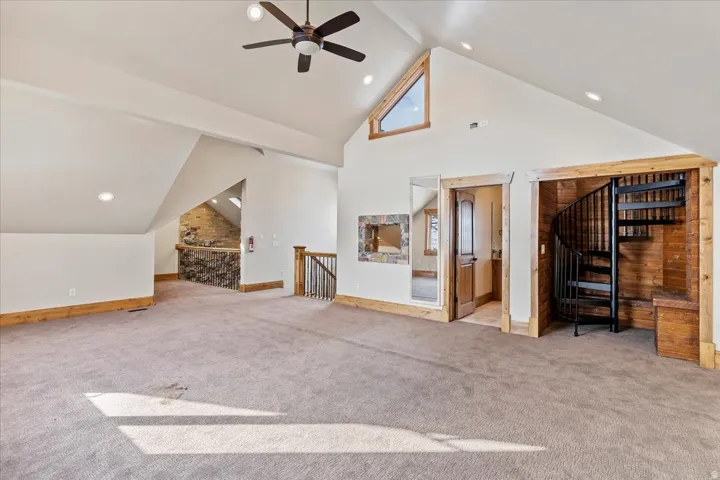 Vaulted ceilings with a ceiling fan, a triangular accent window, recessed lighting, and a spiral staircase with wood-paneled walls