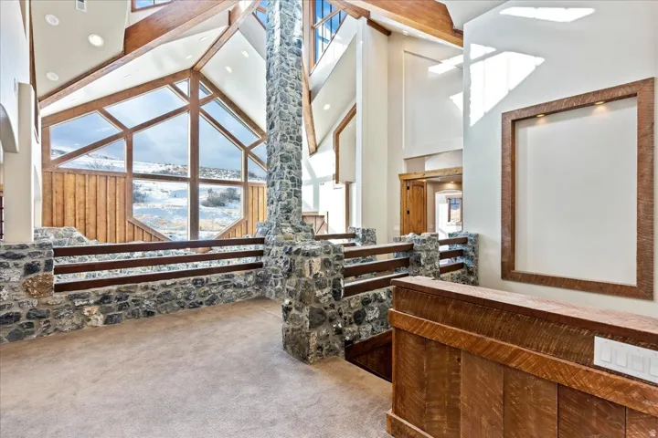Expansive vaulted ceiling with exposed wood beams, large geometric windows, stone pillar, stone and wood railing, and wood-paneled accents