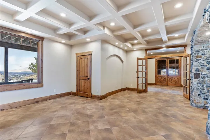 Coffered ceiling with recessed lighting, large picture window, stone accent wall, wood-finish flooring, and double French doors