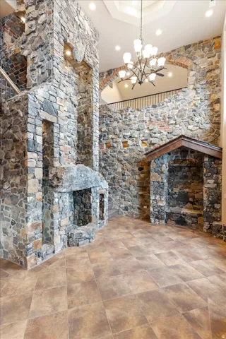 Stone-clad interior walls with a prominent fireplace, tiled flooring, an open upper-level archway, and a multi-tiered chandelier