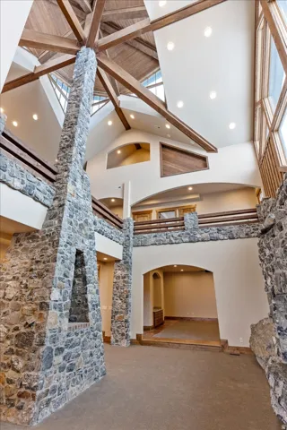 Vaulted wood-beamed ceiling with clerestory windows, stone fireplace with hearth, recessed lighting, and upper-level balcony
