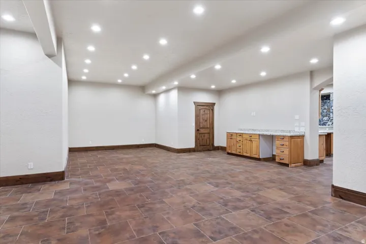 Recessed lighting throughout, tile flooring, built-in cabinetry with stone countertops, wood-finish door, and stone wall accent