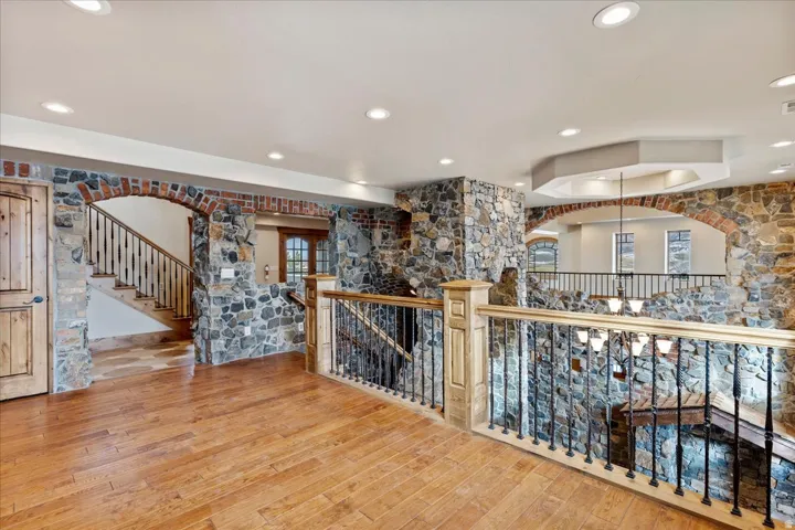Hardwood flooring throughout, stone-clad walls, brick archways, recessed lighting, and a custom wood and wrought iron staircase railing