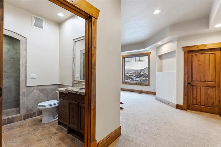 Recessed lighting, wood-finish trim, a bathroom with tiled flooring, a shower with tiled walls, and a vanity with a stone countertop
