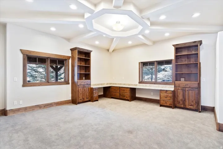 Built-in wood cabinetry, expansive wood-finish desk with a stone countertop, recessed lighting, and a tray ceiling with decorative beams