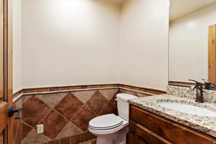 Powder room featuring a wood-finish vanity with a granite-style countertop, undermount sink, and bronze-finish faucet