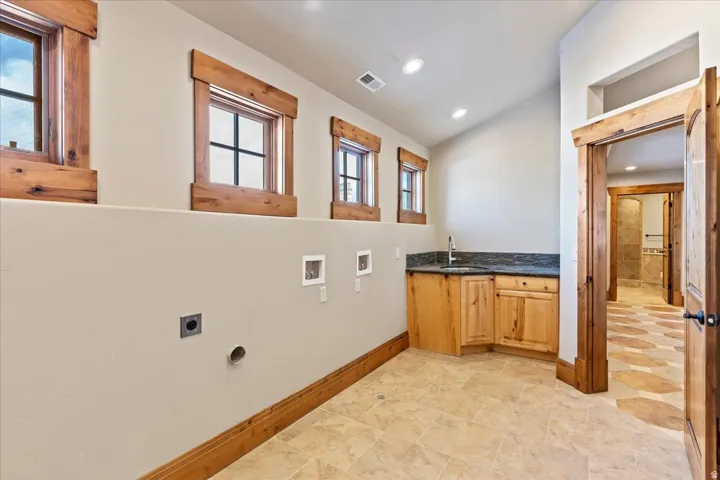 Laundry area with integrated utility sink, wood-finish cabinetry, and dark countertop