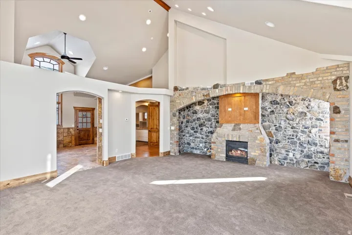 Vaulted ceiling with recessed lighting, stone-clad fireplace, arched doorways, and wood-finish trim