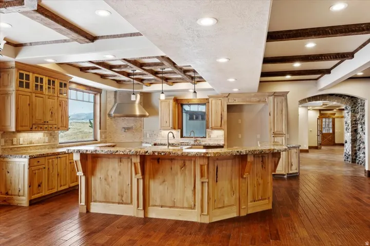 Spacious kitchen featuring wood-finish cabinetry, stone countertops, a large island, and wood-finish flooring