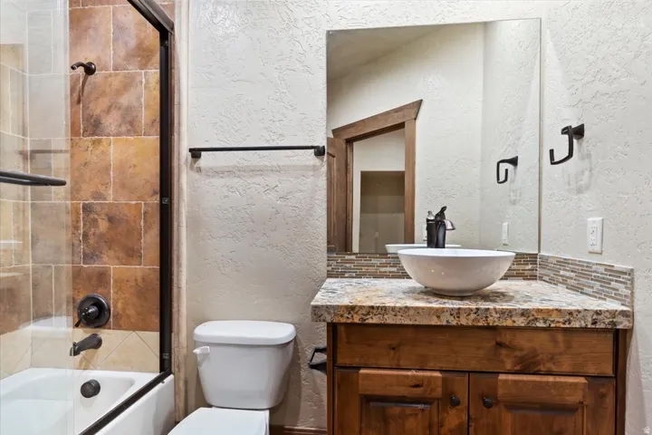 Bathroom featuring a vessel sink, wood vanity, stone countertop, tiled backsplash, and a tiled shower with a glass enclosure