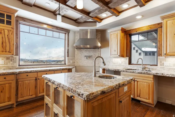 Kitchen featuring wood-finish flooring, natural wood cabinetry, granite countertops, a tile backsplash, and exposed wood ceiling beams