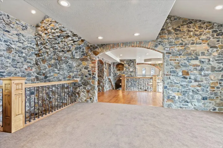 Interior stone wall accents, arched brick doorway, recessed lighting, carpeted flooring, and wood-finish handrailing with iron balusters