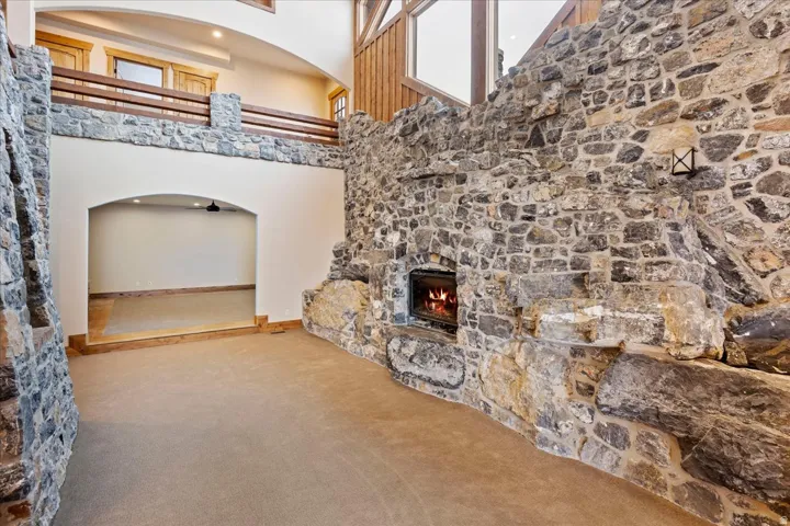 Extensive stone accent walls featuring a built-in fireplace, a stone-faced second-story railing with a wood top, and a recessed archway