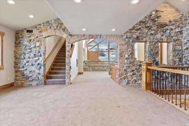 Stone and brick accent walls, arched doorways, recessed lighting, carpeted flooring, and a staircase with wood railing and metal balusters