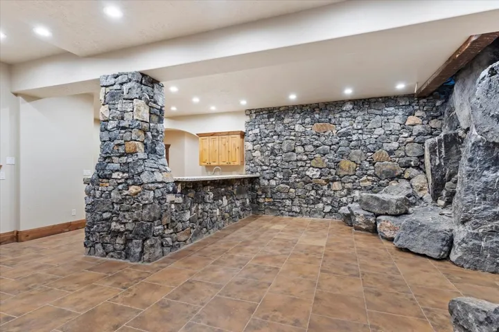 Stone accent wall and column, built-in wet bar with wood cabinetry, recessed lighting, and large format tile flooring
