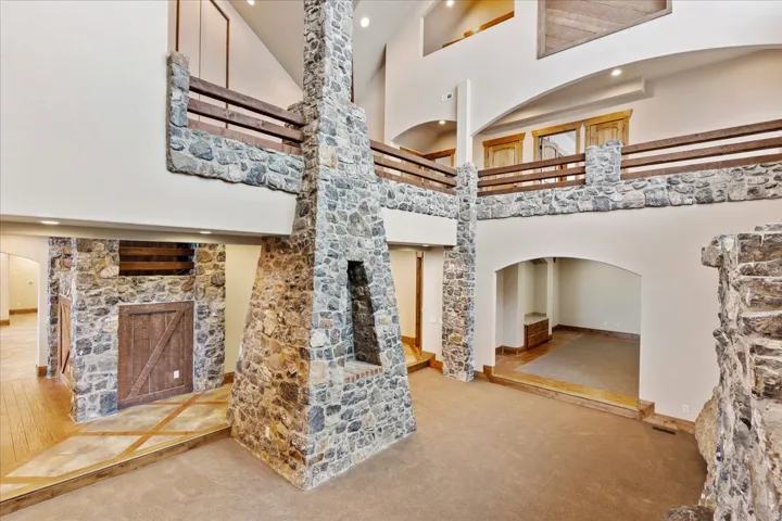Two-story living area featuring a stone fireplace, stone accent walls, vaulted ceilings, and an upper-level balcony with wood railings