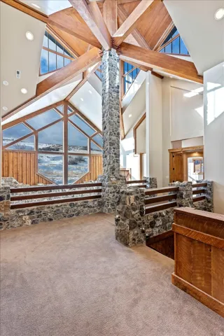 Vaulted wood-beamed ceiling with exposed stone column, multiple windows, stone and wood-finish railing, and recessed lighting