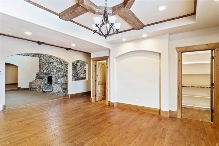 Hardwood flooring, coffered ceiling with wood beams, recessed lighting, arched doorways, and a stone fireplace