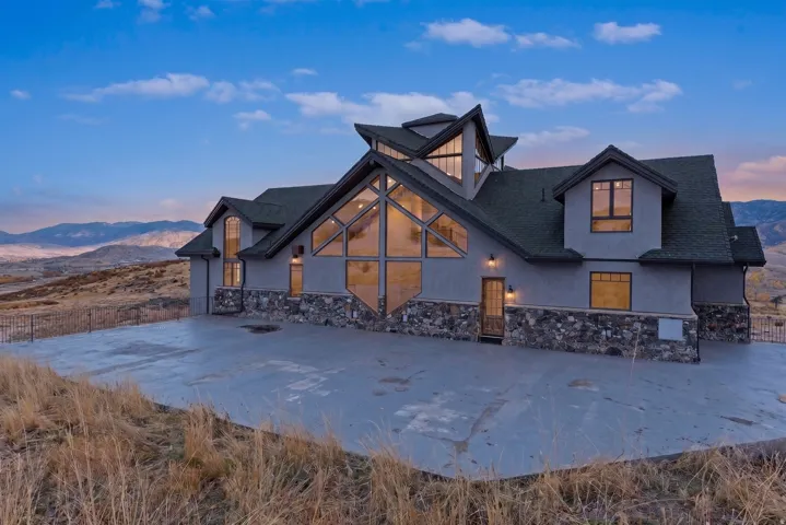 Contemporary architecture with a striking peaked roofline, extensive window walls, a stone and stucco facade, and a concrete approach