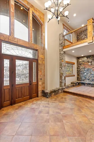 Two-story entry with stone-clad walls, leaded glass double entry doors, a multi-tier chandelier, and a second-story interior balcony with wood railing