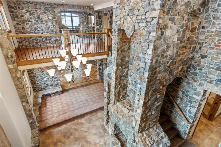 Stone-clad walls with archways, a grand chandelier, wood-finish flooring, and a stone-built fireplace