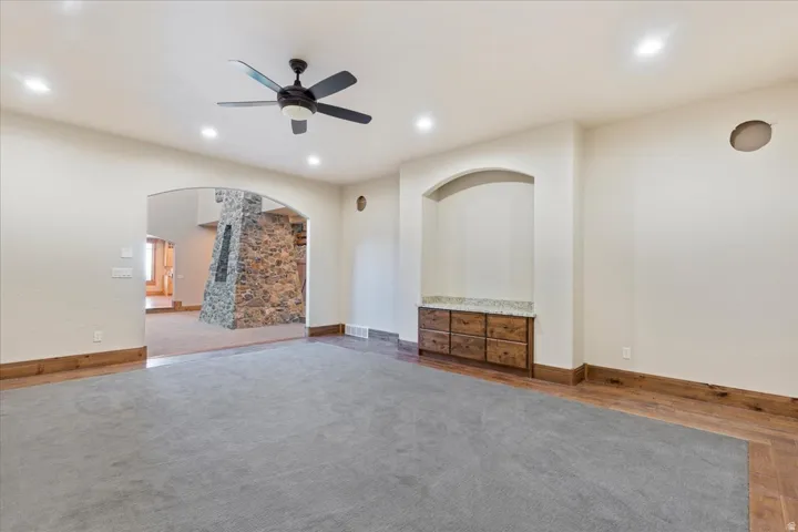 Recessed lighting, ceiling fan, arched doorway, built-in cabinetry with stone-finish countertop, and wood-finish flooring