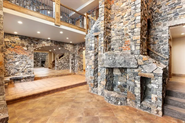 Stone-clad interior walls featuring an integrated fireplace, a second-story landing with wood railing, recessed lighting, and tile flooring