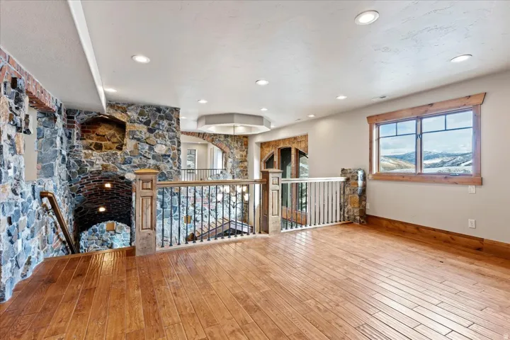 Wood-finish flooring, recessed ceiling lighting, stone accent walls, wood trim window, and wrought iron railings