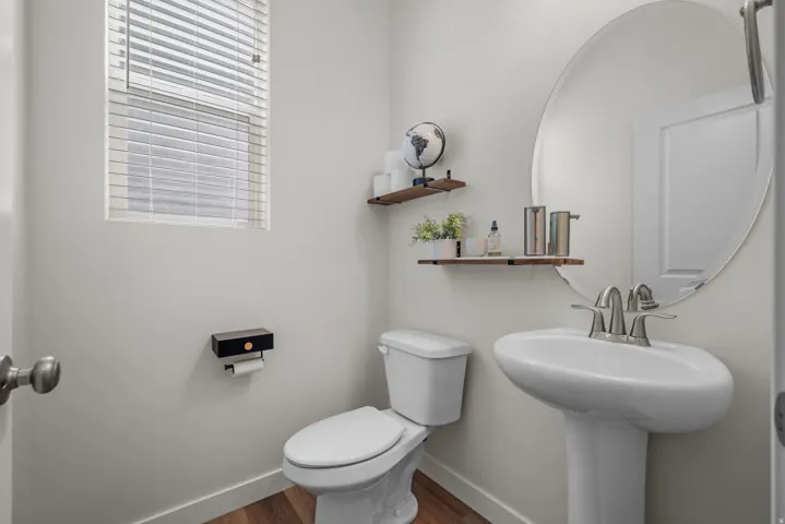 Pedestal sink with chrome fixtures, oval mirror, and wood-finish flooring