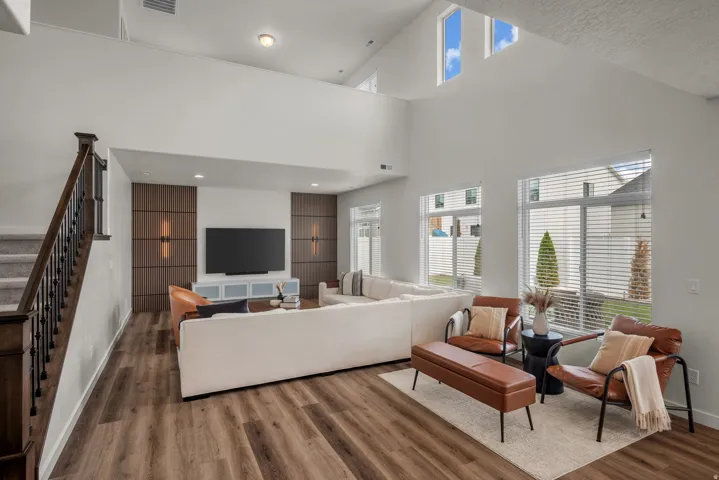 Vaulted ceilings with high transom windows, wood-finish flooring, staircase with dark wood handrail and black iron spindles, recessed lighting, and integrated wall sconces