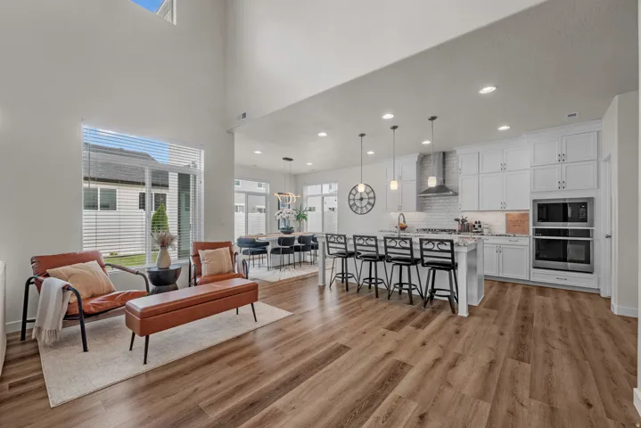 Vaulted ceilings with high windows, wood-finish flooring, white cabinetry, a kitchen island with seating, and stainless steel appliances