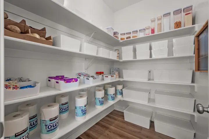 Corner pantry featuring multiple white shelves, a wood-finish flooring, and a white interior