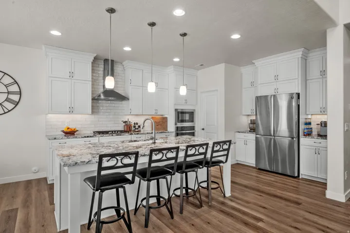 Kitchen featuring white shaker cabinetry, stainless steel appliances, a center island with pendant lighting, stone countertops, and wood-finish flooring