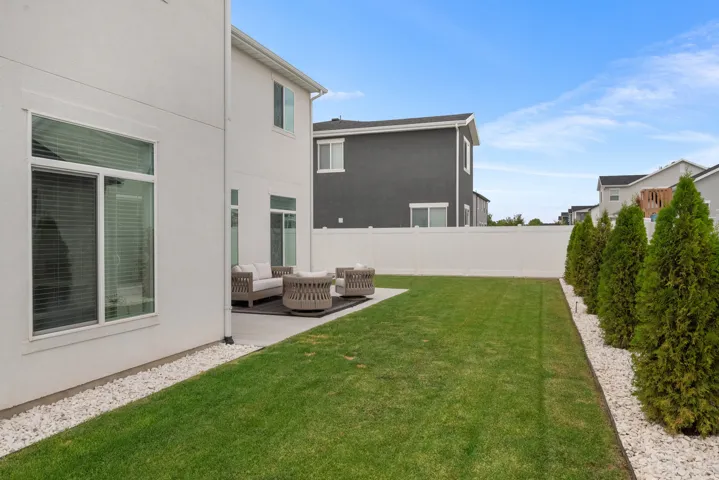 Expansive lawn area with a concrete patio, white vinyl fencing, and a row of evergreen trees