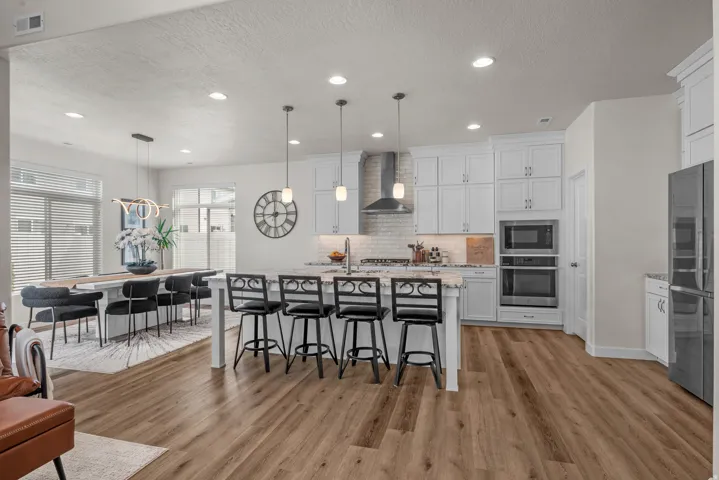 Open-concept kitchen and dining area featuring wood-finish flooring, white cabinetry, a kitchen island with seating, stainless steel appliances, and recessed lighting