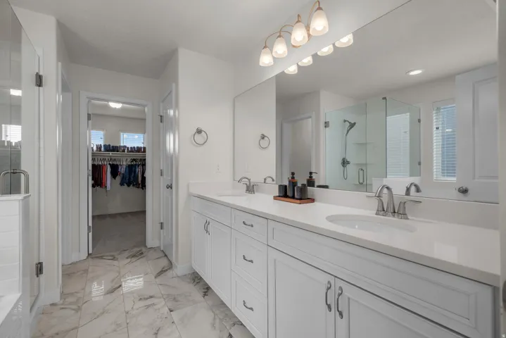 Dual vanity with white cabinetry, polished chrome fixtures, and a large frameless mirror