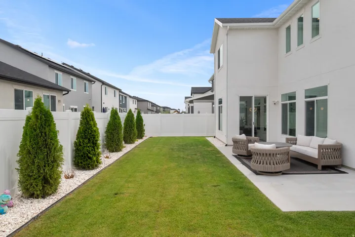 Expansive backyard featuring a manicured lawn, established privacy trees, a white vinyl fence, and a concrete patio