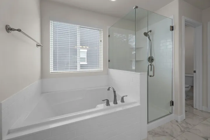 Built-in soaking tub with brushed nickel fixtures, separate glass-enclosed shower with subway tile surround, recessed lighting, and large format floor tiling