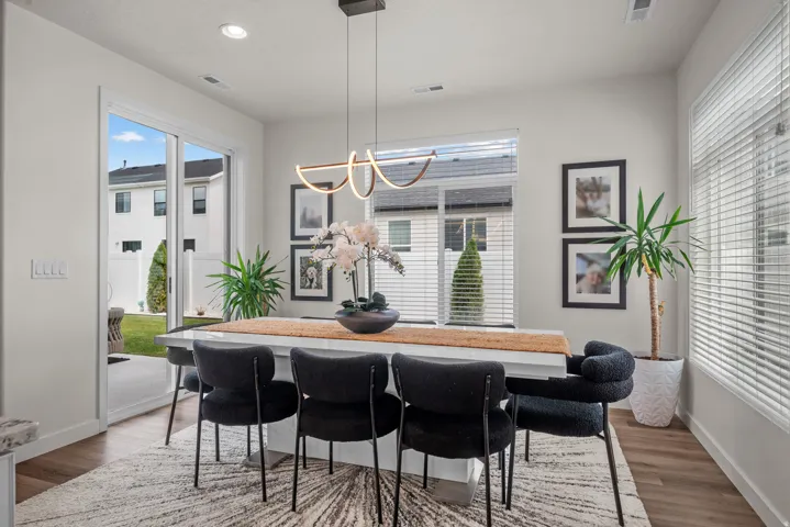 Open-concept dining area featuring wood-finish flooring, a modern linear light fixture, large windows, and sliding glass door access to the backyard with a concrete patio