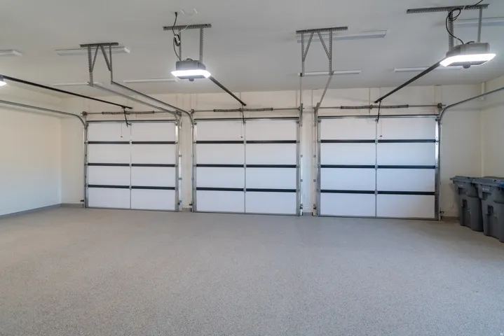 Three individual garage doors, each with an automatic opener, complement the light gray epoxy flooring and overhead lighting