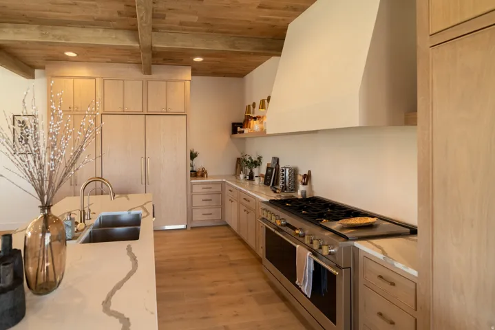Kitchen featuring wood-finish flooring, wood beam ceiling, integrated paneled refrigerator, stainless steel range with griddle, and light-toned cabinetry