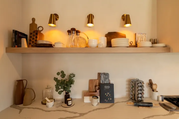Floating wood shelf with integrated wall-mounted sconces, complemented by a light-toned countertop featuring a prominent veining pattern
