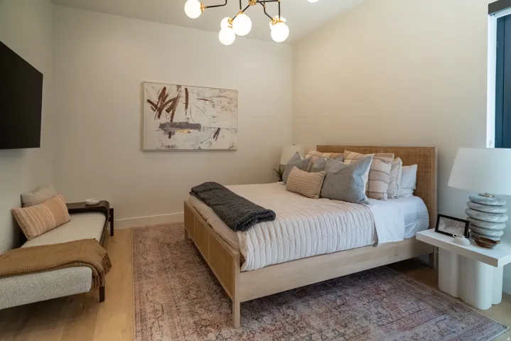 Vaulted ceiling with an attached modern light fixture, wood-finish flooring, and a window with dark trim