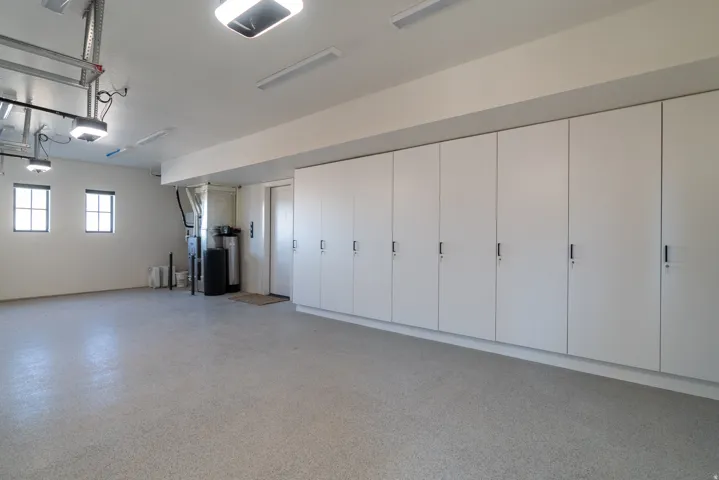 Expansive garage with durable speckled flooring, multiple windows, extensive built-in cabinetry, and overhead lighting