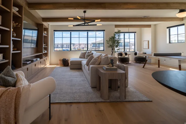 Spacious room featuring wood-finish flooring, exposed ceiling beams, built-in shelving with integrated cabinetry, and multiple large windows with dark frames
