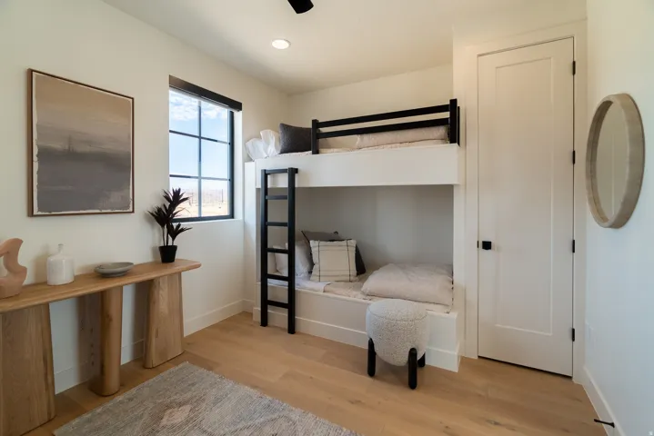 Light wood-finish flooring, white walls, and a built-in bunk bed structure with black railings